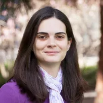 Latina with long hair wearing a light purple scarf and purple shirt smiling against a natural background