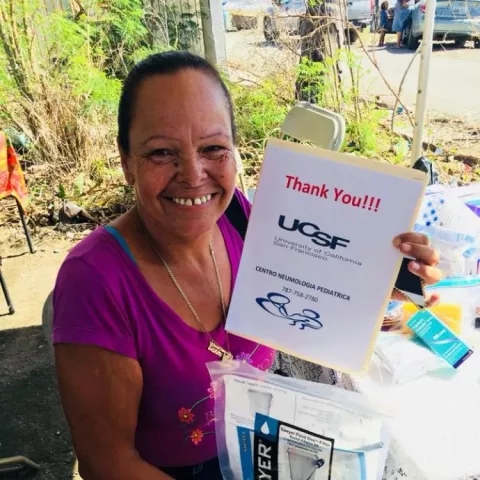 woman in pink shirt holding water filter and a thank you sign in Puerto Rico after hurricane Maria