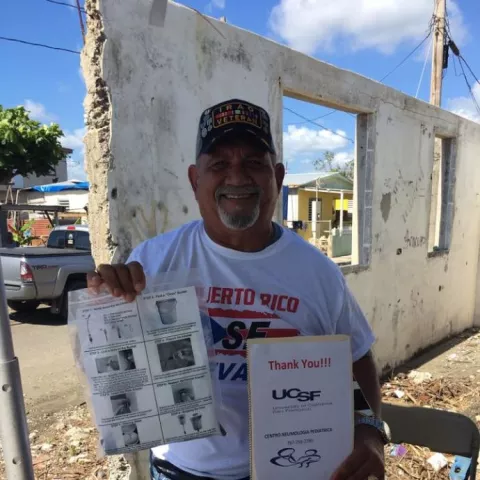 man in baseball cap holding water filter and a thank you sign in Puerto Rico after hurricane Maria