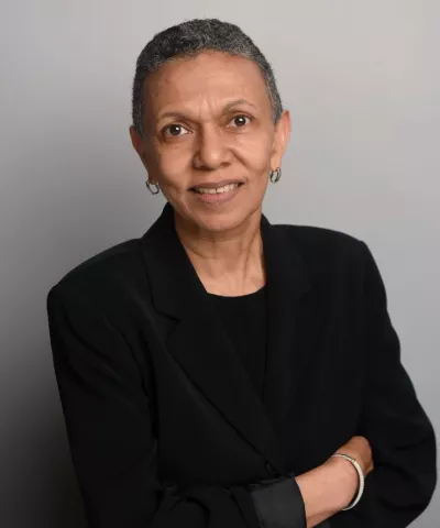 older ethnic female with short hair in a black suit smiling against a white background