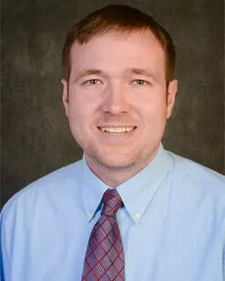 professional headshot of a smiling man in a red tie and blue shirt