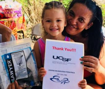 Mother and daughter holding a water filter and a sign thanking UCSF
